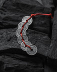 Silver coin bracelet with red cord on dark stone background