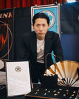 Man in a black suit standing behind a display of jewelry and a certificate.