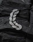 Silver coin necklace on a dark stone surface