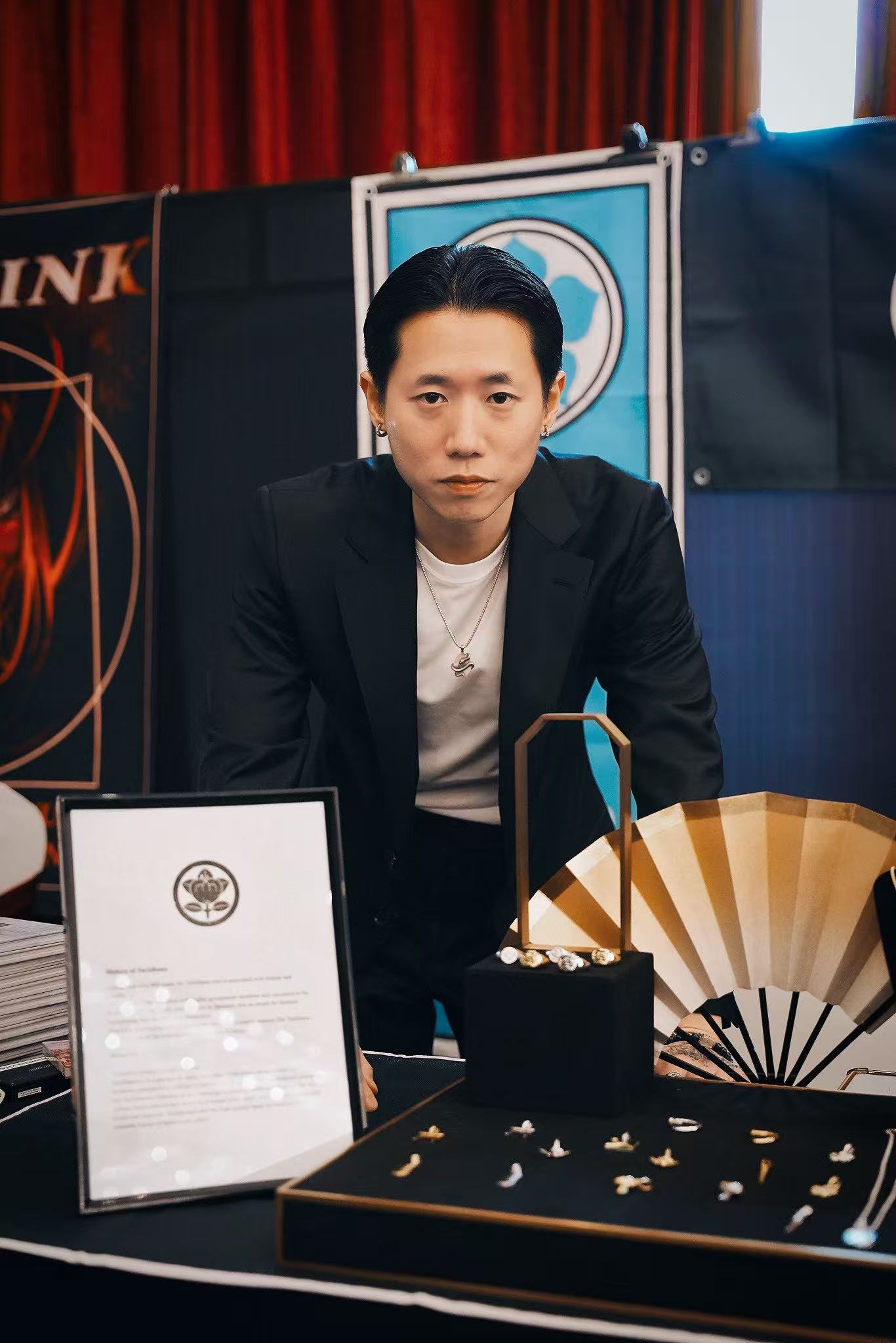 Man in a black suit standing behind a display of jewelry and a certificate.